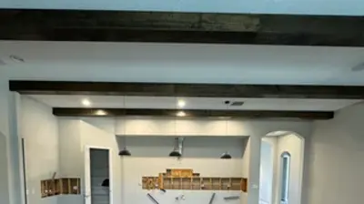 A large room under renovation. Dark wood ceiling beams are installed, with a concrete floor ready for finishing and wall cut-out Photo