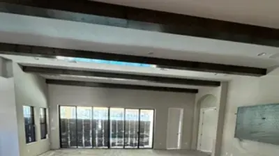 An empty, large room with concrete floors, exposed dark ceiling beams, and multiple windows. Photo