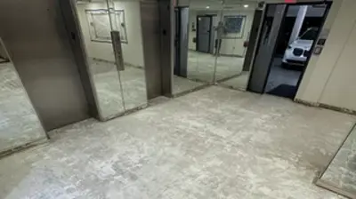 A room undergoing renovation, featuring a rough concrete floor and mirrored walls reflecting an interior lobby. Photo