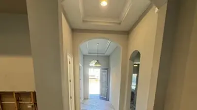 A long hallway in a house under construction, featuring arched doorways, a tray ceiling, and dusty floors with primed walls. Photo