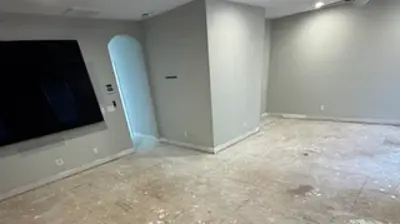 A room undergoing renovation with a dusty, unfinished floor covered in white debris. Photo