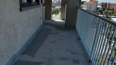 View from a long, concrete apartment or hotel balcony with a metal railing, overlooking other buildings and a parking lot. Photo
