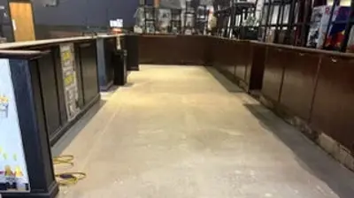 An empty commercial space featuring a long concrete floor between dark wooden counters. Photo