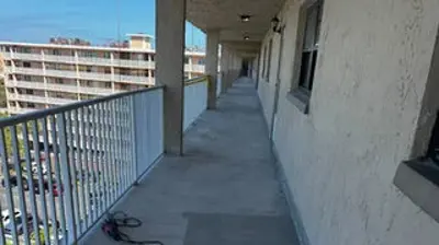 View from a long, concrete apartment or hotel balcony with a metal railing, overlooking other buildings and a parking lot. Photo