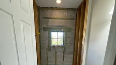 An unfinished bathroom or shower room features concrete block walls, a small window, and exposed studs. Photo