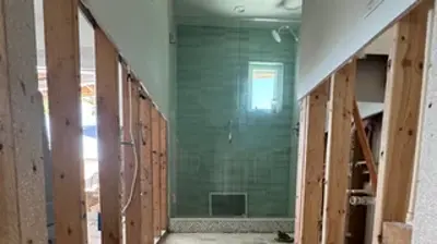 A home renovation project showing a hallway with exposed wooden studs and a dusty concrete floor. Photo