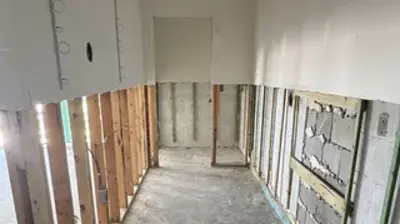 A room undergoing renovation with partially removed walls, showing exposed wooden studs and concrete blocks. Photo