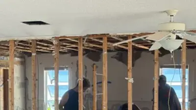 An indoor renovation shows three men working amidst exposed wooden studs and debris. Photo