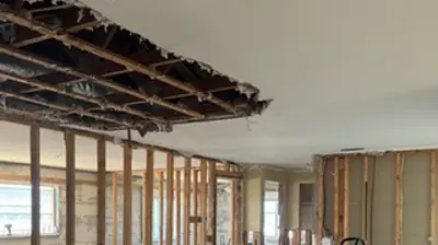 An interior space during renovation, revealing exposed wall studs, a damaged ceiling, and construction debris with a wheeled car Photo
