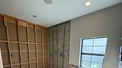 A room under construction showing exposed wall studs, concrete blocks with plumbing pipes, and a window. Photo