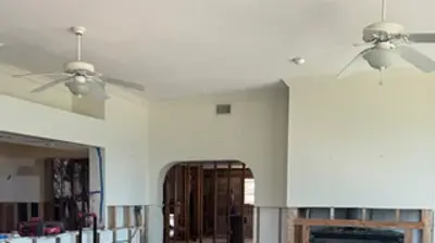 An interior view of a house during water damage restoration, featuring protective floor covering, exposed wall studs, and variou Photo