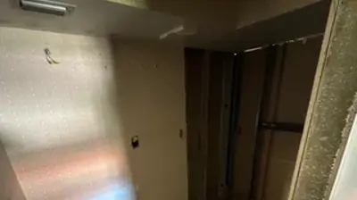 An unfinished room with bare walls and a concrete floor, featuring visible plumbing on the left wall. Photo